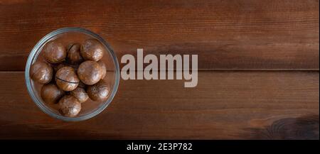 Banner with unpeeled macadamia in bowl on dark wooden table. Top view, space for text Stock Photo