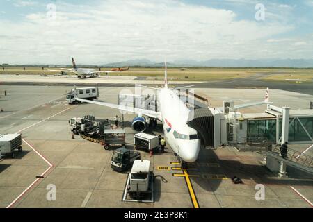 British Airways Comair flight at a passenger terminal point being loaded for a domestic flight with vehicles and employees working on the tarmac Stock Photo