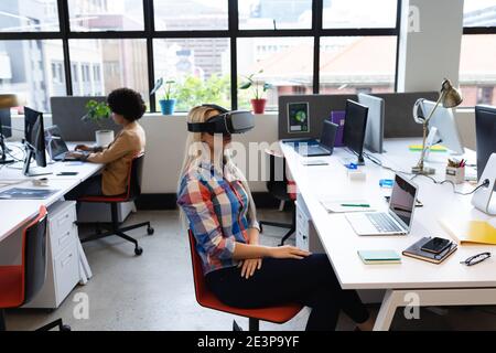Caucasian businesswoman sitting at desk in office wearing vr headset Stock Photo