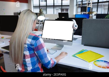 Caucasian businesswoman sitting at desk in creative office using desktop computer Stock Photo