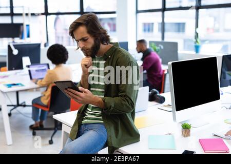 Caucasian businessman leaning on desk using tablet computer in creative office Stock Photo