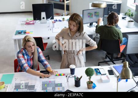 Two diverse businesswomen looking at blueprints and discussing in creative office Stock Photo