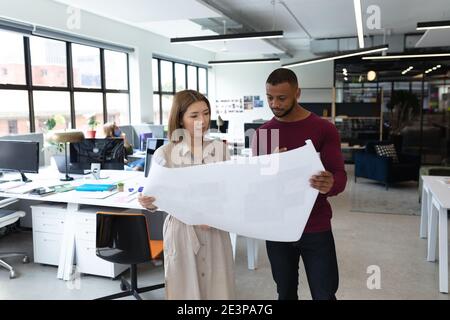 Diverse male and female colleague looking at blueprints and discussing Stock Photo