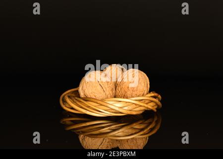 Three whole brown natural ripe tasty walnuts on a black background, with a wreath of wicker vines. Stock Photo