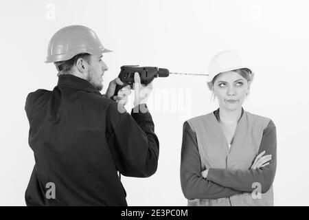 Builder, repairman makes hole in female head. Woman with bored face in helmet ignoring husband annoying her. Marriage issues concept. Man with drill tool drills head of woman, white background. Stock Photo