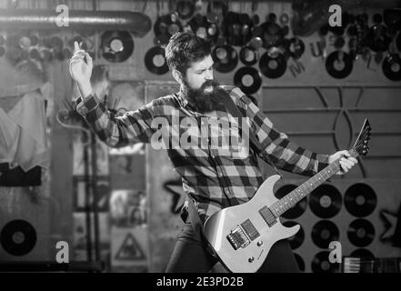 Musician with beard play electric guitar. Man with shouting face play guitar, singing song, play music, music club background. Frontman concept. Musician full of energy, soloist, singer. Stock Photo