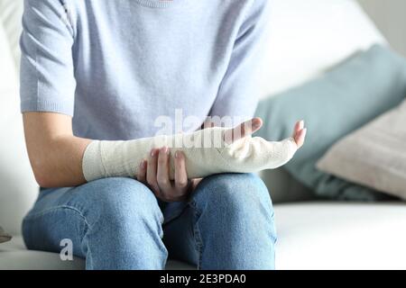 Close up portrait of a disabled woman grabbing her painful bandaged arm on a couch at home Stock Photo