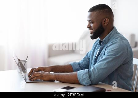 Smiling Millennial African American Man Working With Laptop At Home Office Stock Photo