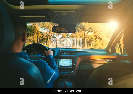 Young man driving car at sunset. Man using navigation system while driving a car Stock Photo