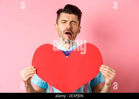 Valentines day concept. Sad and lonely man feeling heartbroken, being rejected, showing big red heart cutout and crying from break-up, standing on Stock Photo