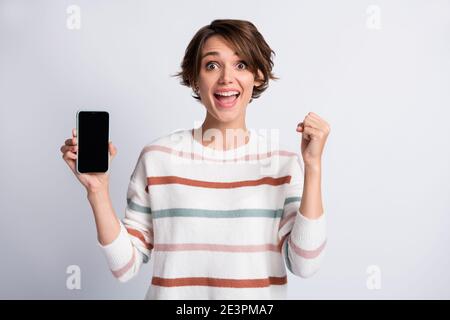 Photo of funny impressed woman dressed striped pullover holding modern device rising fist isolated grey color background Stock Photo