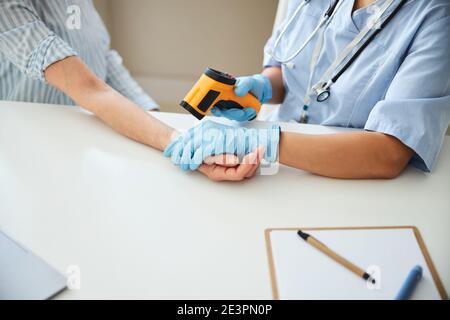 Medic using a temperature gun on an aged patient arm Stock Photo