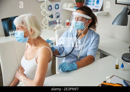 Medic with a stethoscope hearing an old lady breathing Stock Photo