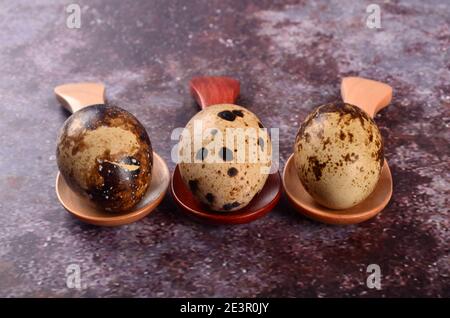 Three quail eggs in small wooden spoons, gray background Stock Photo