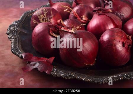 Several red onions on a metal plate, purple background. Still life with red onions Stock Photo
