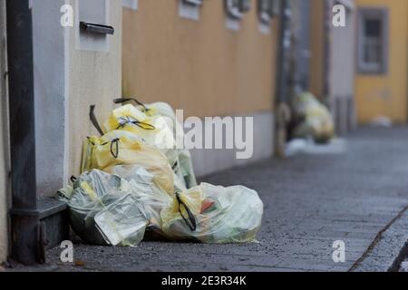 Yellow plastic sacks containing plastic garbage piled up near front-doors on sidewalk of street for waste collection in old town with stone houses Stock Photo