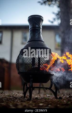 A chimenea during the day burning some wood in a back garden. Stock Photo