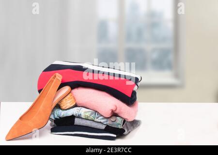 A stack of folded sweaters, a pair of jeans and a elegant brown shoe on table over blurred curtain background. Advertising for fashion and accessories Stock Photo