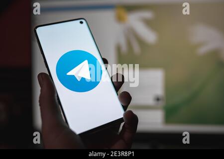 Man holding a smartphone with Telegram messenger chat app logo displayed on the screen in front of the Telegram web version Stock Photo