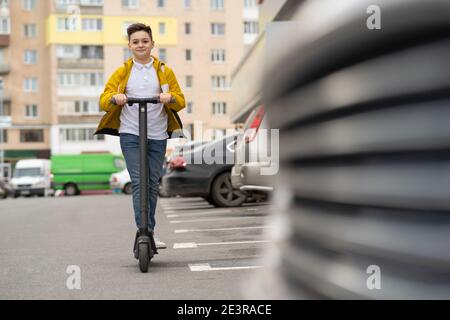 Joyful teenager rides on electric scooter down street Stock Photo