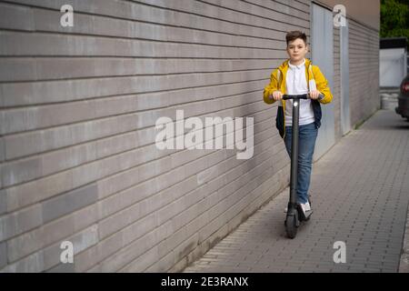 Handsome teenager rides on electric scooter down the city street Stock Photo