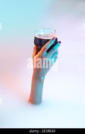 Touch. Close up female hand gesturing from the milk bath with soft white glowing in neon light. Copyspace for advertising. Modern neoned colors, foam. Holding stout dark beer glass. Drinks, alcohol. Stock Photo