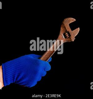 A man's hand in a blue glove holds a rusty wrench. Close-up Stock Photo