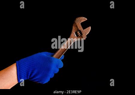 A man's hand in a blue glove holds a rusty wrench. Close-up Stock Photo