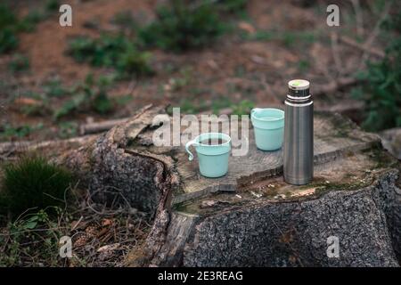 A thermos with tea and two cups outside on a tree stubb Stock Photo