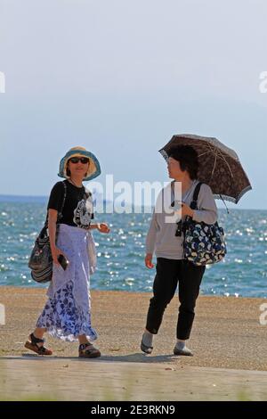 Two Chinese women walking on a sea street in Thessaloniki Stock Photo