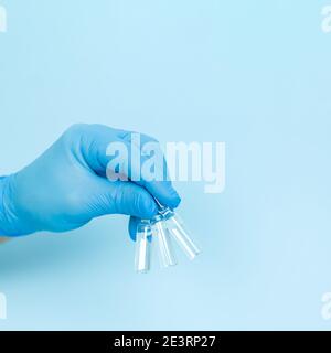 Doctor's hand in glove holding three medical glass ampoules on blue background Stock Photo