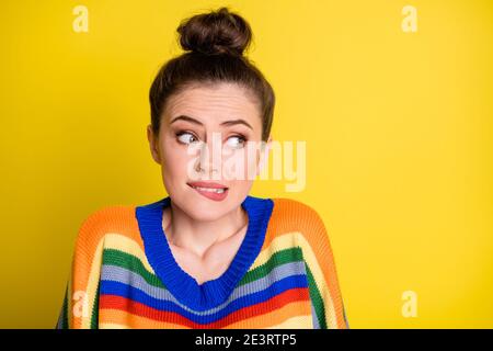 Photo of cute sweet brunette girl looking empty space bite lips wear rainbow sweater isolated on bright yellow color background Stock Photo