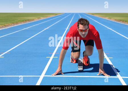 Starting to run athlete sprinter ready to run on blue tracks in track and field event race at start line at outdoor stadium. Focus and motivation Stock Photo