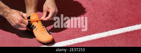 Running shoe at start line success challenge competition banner. Athlete fit man getting ready for run race tying running shoes. Panoramic on red Stock Photo