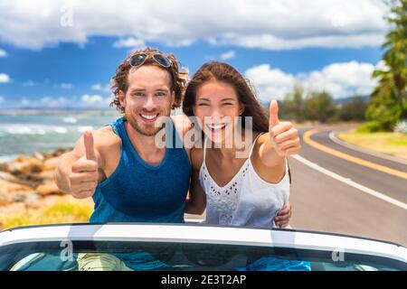 Car happy road trip young drivers driving in convertible cabriolet car. Smiling couple doing thumbs up on summer holiday road trip in new car