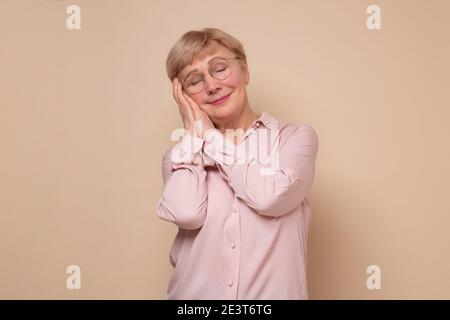 Mature woman sleeping tired dreaming and posing with hands together with closed eyes. Studio shot Stock Photo