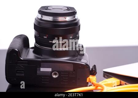 Digital photo camera connected to laptop with USB orange rolled cable. Stock Photo