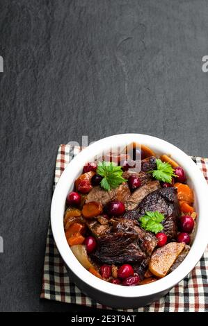 Braised  beef with cranberries in clay bowl on black stone background Stock Photo