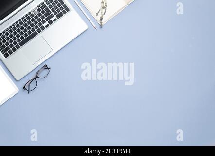 Business space on a blue background. Top view of laptop, notepad and glasses. copy space. Stock Photo
