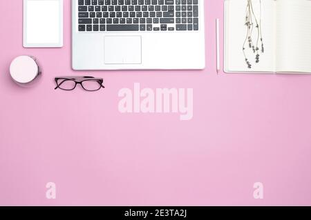 Stylish work feminine business desk with laptop and modern office attributes. Top view. Copy space. Flat space. Pink background. Stock Photo