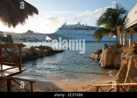 The sunset view of a tiny beach surrounded by restaurants in front of moored cruise ships on Cozumel island (Mexico). Stock Photo
