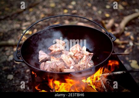 Cooking pilaf in Asian cauldron on the grill outside in forest. Selected focus. Stock Photo