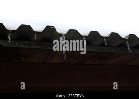 The snow on the roof melts and forms ice icicles. Stock Photo