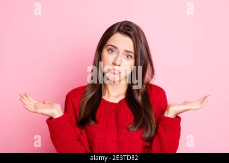 Photo portrait of sad unhappy girl keeping both hands near shoulders like doesn't know wearing red sweater isolated pink color background Stock Photo