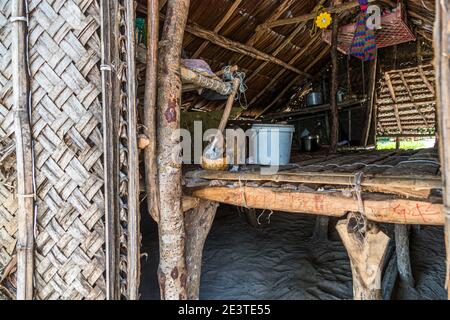 A puppy sniffs at a halved coconut shell on the bamboo platform of a traditional hut on Panasia Island, Milne Bay Province, Papua New Guinea, colorful toys hanging from the woven roof in the background. Stock Photo