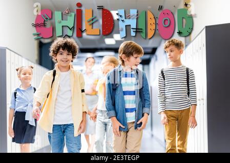 multicultural schoolchildren walking along school corridor with teacher on background, childhood illustration Stock Photo