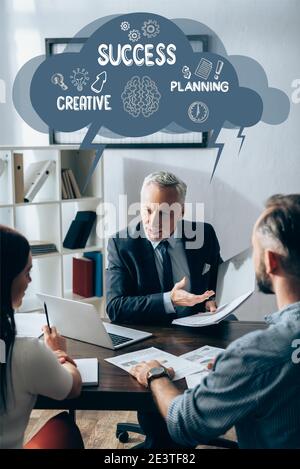 Investor in formal wear pointing at paper folder near laptop and business partners on blurred foreground, success, creative and planning illustration Stock Photo