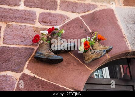 Old hiking shoes using as flower pot hanging stone wall house. Hiking background. Lifestyle, natural leaving, travel, sustainable consumption concepts Stock Photo