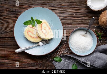 Delicious dessert, coconut roulade slices filled with vanilla and rum buttercream on rustic wooden background Stock Photo