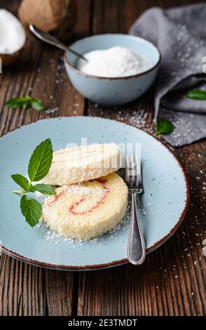 Delicious dessert, coconut roulade slices filled with vanilla and rum buttercream on rustic wooden background Stock Photo